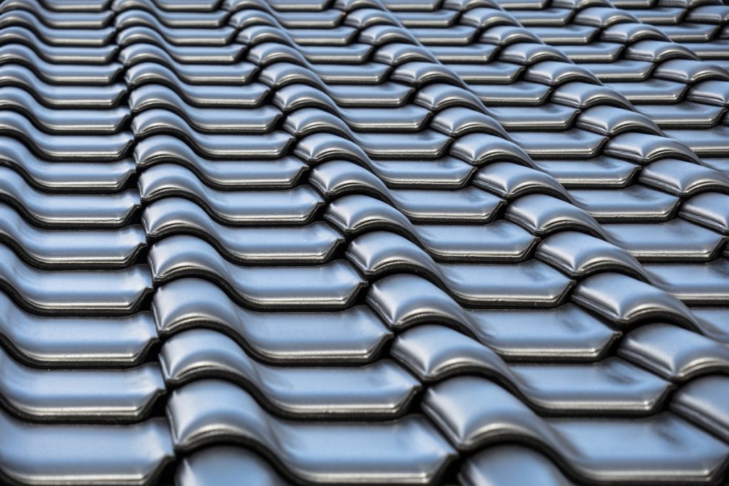 Zbliżenie na dachówki ułożone na dachu, przedstawiające estetyczne i trwałe wykończenie, symbolizujące wybór jakościowych materiałów przy montażu dachu.