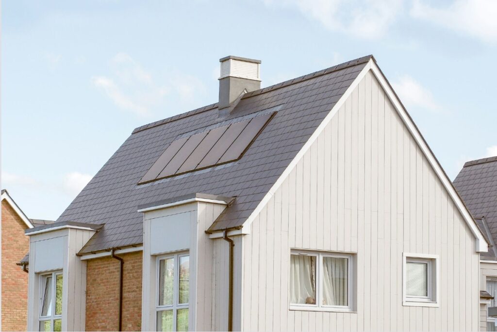 Nowoczesny dom z dachem w kolorze antracytowym, zintegrowanymi panelami fotowoltaicznymi i jasną elewacją.